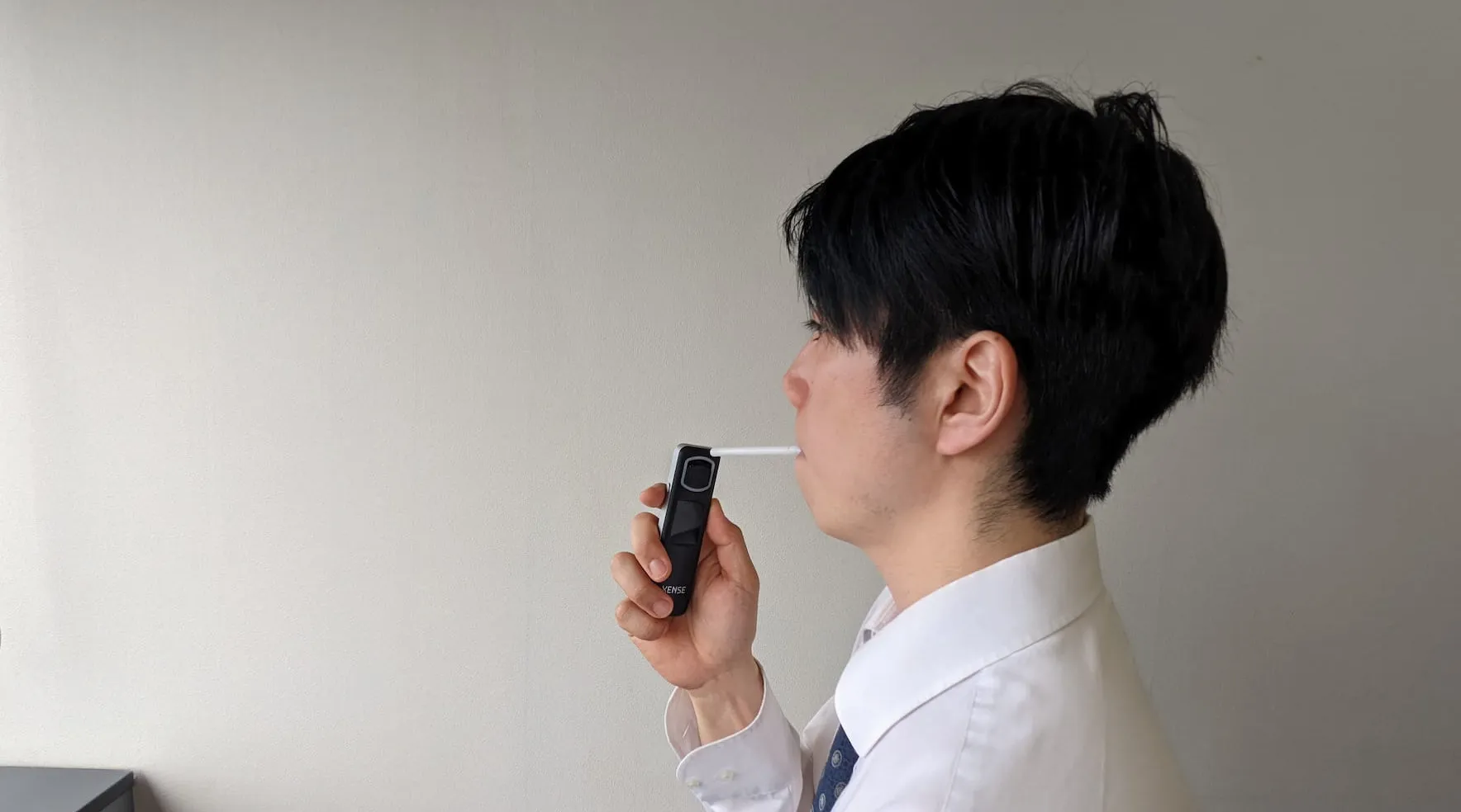 ストローを取り付けたアルコールチェッカーに息を吹きかける様子