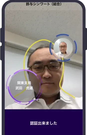 スマートフォンの顔認証画面で顔が円で囲まれ、氏名とともに「認証出来ました」と表示されている